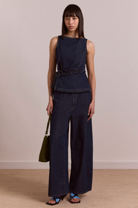 Woman wearing a sleeveless denim top and wide-leg jeans against a plain background